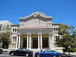 A two-story brick building faces the street. In its center is a portico, projecting forward from the rest of the building, and supported by four sets of white double columns, front and back. Stairs lead up to the columns, and between the columns are three sets of brown double doors. Carved into the entablature are the words "My House Shall Be Called A House Of Prayer for All People", all in capitals. On each side of the entrance are windows set into the wall, two on the first floor and three smaller on the second floor.