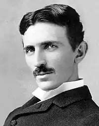 A black and black picture of a moustachioed dark haired man looking at the camera.