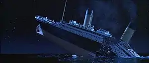 The Titanic about to sink into the ocean, with the ship breaking into two parts and with smoke still coming out of the funnels.