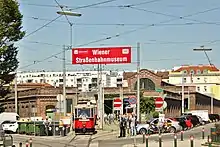 A red historic tram leaving a large brick tram depot, now the Vienna Transport Museum, with a large red sign reading "Wiener Straßenbahnmuseum"