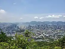 Trees in foreground, urban buildings and harbour in midground, sea and islands in background