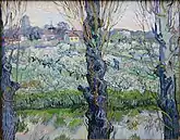 A close view of three blossoming trees behind which can be seen a large orchard and field in which a man is working, a village filled with buildings and houses in the background, under a bright sky