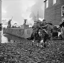 two men each side of a wounded man, helping him towards a boat docked between houses